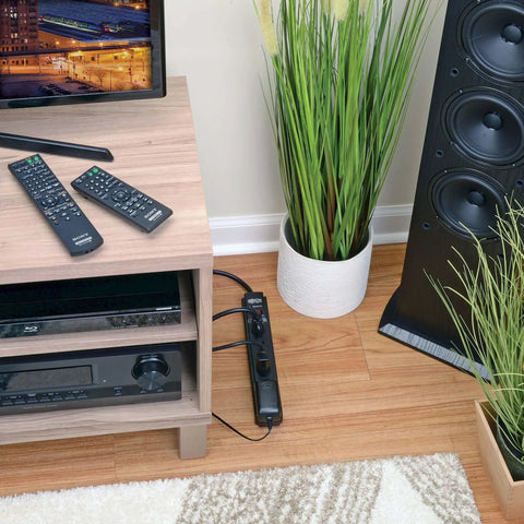 Six Outlet Surge Protector Power Strip With Six Foot Extension Cord Delivers 900 Joules Of Surge Protection, 15 Amp Circuit Breaker, UL Certified, Black on floor next to media console in living room