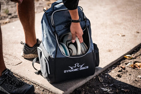Person placing discs into Trooper Disc Golf Backpack, black, holds 18 plus discs, lightweight yet tough bag for beginners, spacious gear carrier