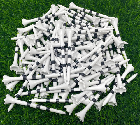 Pile of Three And A Quarter Inch White Golf Tees With Black Stripes Pack Of 50 Durable Plastic Tees With Six Prong Cup on grass