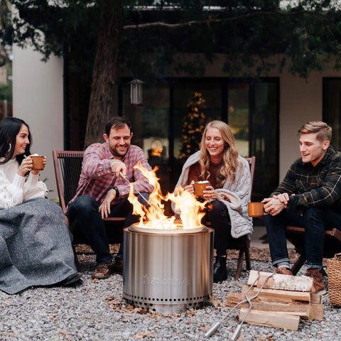 Group gathered around a Bonfire Stand For Smokeless Fire Pits And Outdoor Fireplaces Durable 304 Stainless Steel Heat Resistant Portable Elevated Fire Pit Accessory That Keeps Decks And Grass Safe While You Camp Or Grill in a modern backyard.