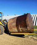 Forklift with yellow pallet forks lifting a large rusted steel drum outdoors