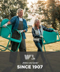 Two women wearing work gloves carrying outdoor chairs in a field at sunset