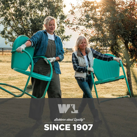 Two women wearing work gloves carrying outdoor chairs in a field at sunset