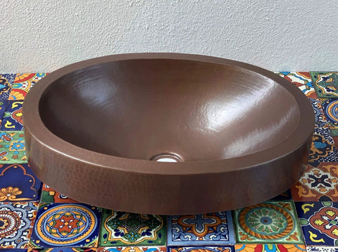 16 By 13 Inch Oval Skirted Vessel Copper Sink Hand Hammered Pure Copper Brown Finish For Modern Bath Semi Recessed Vessel One And A Half Inch Drain Opening Eighteen Gauge Handmade In Mexico CPS10 on colorful tile surface