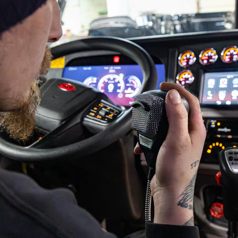 Driver using 636LSE 4-Pin Noise Canceling CB Microphone for Close-Talk Handheld Use, XLR Silver Anniversary Edition in vehicle cabin.