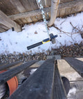 Sledgehammer hanging on a chain above a snowy yard next to a wooden fence, viewed from above