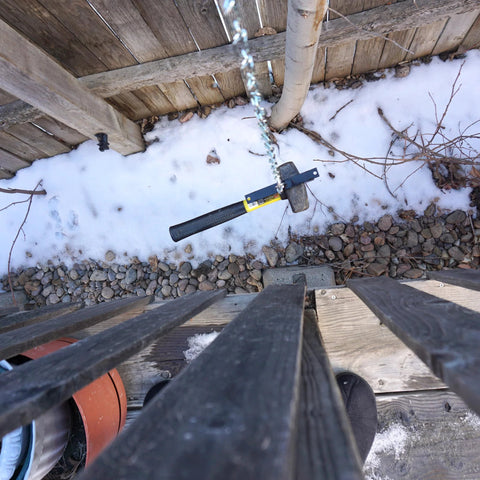 Sledgehammer hanging on a chain above a snowy yard next to a wooden fence, viewed from above