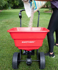 Deluxe Heavy-Duty Walk-Behind Commercial Broadcast Spreader With 80 Lb Capacity being filled with lawn treatment on grass