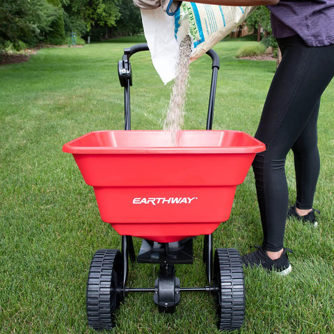 Deluxe Heavy-Duty Walk-Behind Commercial Broadcast Spreader With 80 Lb Capacity being filled with lawn treatment on grass