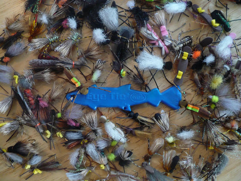 Eye Tie Fly Threader With Magnetic 3 Funnel System For Hook Sizes 3 To 24 surrounded by assorted fishing flies on wooden surface