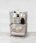 Small Stackable Wire Baskets For Pantry And Counter Organizer With Raised Feet And Handles Stacking Fruit Bin For Vegetables Potatoes Onions Storage In Satin Nickel Finish on counter filled with toiletries.