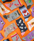 Variety of novelty crew socks with playful designs on orange background, including patterns like fox, panda, and roller skates.