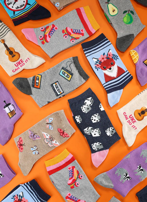 Variety of novelty crew socks with playful designs on orange background, including patterns like fox, panda, and roller skates.