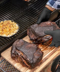 Grill Ready Disposable BBQ Gloves Kit With 50 Nitrile Gloves used to handle smoked meat next to a grill with corn dish