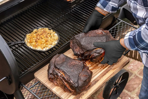 Grill Ready Disposable BBQ Gloves Kit With 50 Nitrile Gloves used to handle smoked meat next to a grill with corn dish