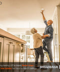 Elderly couple installing LED recessed downlight in kitchen, using ladder for ceiling access.