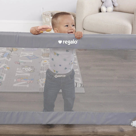 Extra Wide Mesh Baby Gate For Doorways And Hallways Expands From 27.5 To 50 Inches 28 Inches Tall Pressure Mounted For Toddlers And Pets Includes Rubber Bumpers Gray with toddler behind mesh in living room.