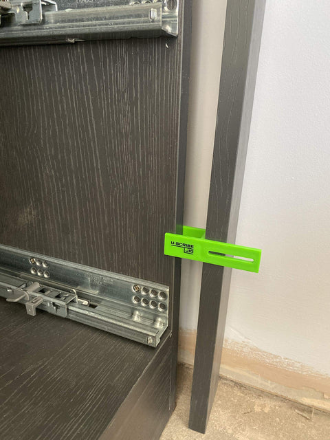 Green scribe jig from Pro Grade Scribe Jig Installers Set for precise cabinet fitting, showing placement against dark wood surface.