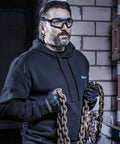 Man wearing anti-fog safety goggles with clear lens and adjustable elastic headband, in a workshop setting holding chains.
