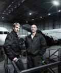 Two mechanics in a hangar with airplanes, wearing black uniforms and holding Kraftform Plus 334 SK Pro Grade Six Piece Screwdriver Set.