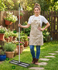 Person holding 30x10 Inch Lawn Leveling Rake with Adjustable 80 Inch Handle in garden, aluminum rollers and stainless steel build visible