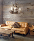Brown Adjustable Resin Antler Three Light LED Chandelier hanging in rustic living room with wooden walls and leather sofa.