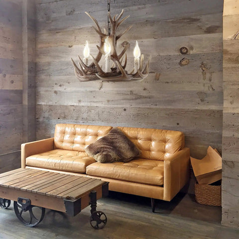 Brown Adjustable Resin Antler Three Light LED Chandelier hanging in rustic living room with wooden walls and leather sofa.