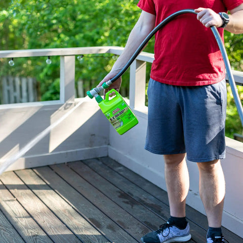 Person using EZ Deck Fence And Patio Wash 64 Oz Mold And Mildew Killer with hose end sprayer on wooden deck.