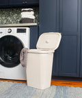 Slim Laundry Hamper With Lid 50L Capacity Clothes Basket in ivory plastic with a wicker look in a laundry room with washing machine.