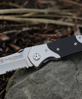 Knockout 8 Inch Folding Knife Packing A 3.3 Inch Drop Point Serrated High Carbon Stainless Blade And G10 Grip Handle on a stone.