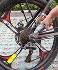 Person using a tool on a bicycle's rear wheel and gear system outdoors on a paved surface.