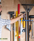 Man organizing tools on 9 Slot Wall Mounted Garden Tool Rack With 6 Hooks In Blue Steel, Space Saving Tool Organizer For Shed Or Garage, Heavy Duty Hanger System To Tidy Up Tools, Rakes, Shovels And More.