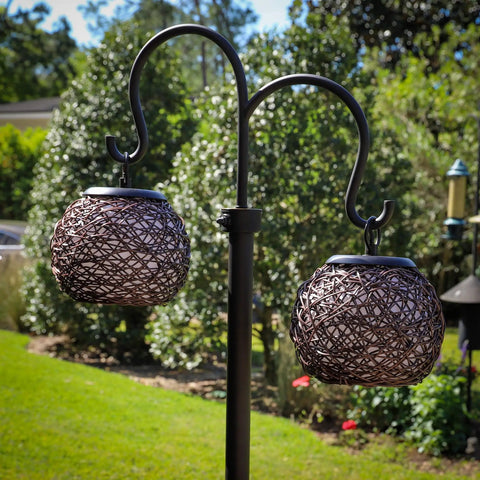 Castillo Outdoor Floor Lamp With Oil Rubbed Bronze Highlight Finish with dual suspended woven rattan shades in a garden setting.