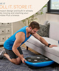 Man storing Rumblex Plus 4D Vibration Plate Exercise Machine With Whole Body Vibration under couch, showing compact design.