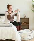 Woman folding laundry in a bedroom with a 50L Laundry Hamper Set With Built In Comfort Handles 3 Pack White Plastic Baskets With Ventilation Holes