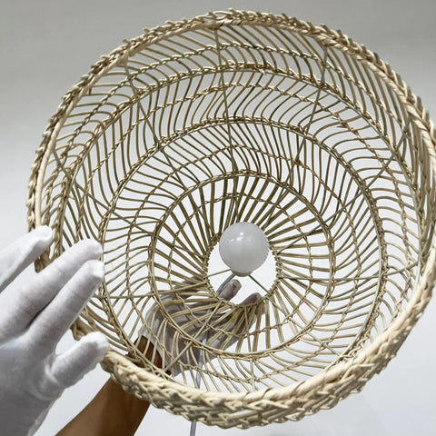 Hands holding beige bamboo pendant light boho style with rattan wrapped shade, view of bulb socket, soft warm glow for kitchens.