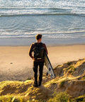 Person with surfboard wearing 25L Waterproof Surf Backpack For Adventure With Roll Top Closure at cliff overlooking beach