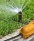 Heavy Duty Outdoor IP44 Protective Case For Wired Connections Keeps Plugs And Sockets Dry Safe From Dirt And Damage Tough As Nails Weather Ready Rugged Housing For Extension Cords And Outdoor Equipment positioned by a garden sprinkler.