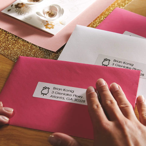 No Sweat White Mailing Address Labels For Slick Office Packing on pink envelope with hand, ideal for organizing shipments.