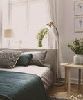 Dimmable Floor Lamp With Sturdy Base For Over Chair Reading in a bedroom, brass finish, providing ambient light next to a bed with cushions.