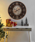 Killer Twenty Four Inch Oversized Wall Clock Featuring Real Moving Gears Heavily Distressed Antique Gold Dial Bold Roman Numerals above a desk with gifts.