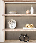 Taupe Metallic Grasscloth Peel And Stick Wallpaper Roll Featuring Faux Woven Texture With Subtle Shimmer on wall behind decorative shelves.