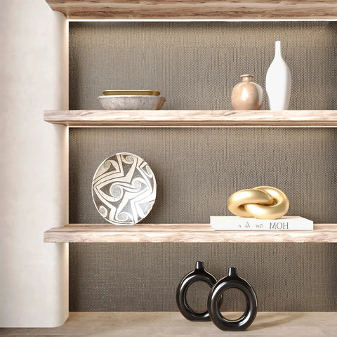 Taupe Metallic Grasscloth Peel And Stick Wallpaper Roll Featuring Faux Woven Texture With Subtle Shimmer on wall behind decorative shelves.