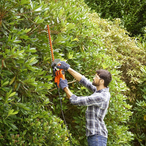 Man using Heavy Duty Electric Hedge Trimmer With 420 Watt Motor And 45CM Cutting Blade for trimming bushes in garden.