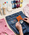 Using Speedweve Style Darning Loom Kit With 14 And 28 Hook Looms to mend jeans, surrounded by color threads and darning tools.