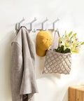 Hella Sturdy Wall Mount Coat Rack Featuring Heavy Duty Double Steel Hooks For Backpack Storage And Rust Proof Coating For Mudroom Storage That Handles Maximum Load Zero Fuss with beige jacket, yellow cap, and floral bag.