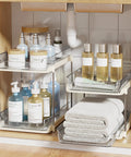 No Fuss Slide Out Two Tier Under Sink Organizer With Reconfigurable Dividers Stackable Pantry Storage Rack In Warm Beige with towels and bottles.