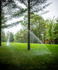 Heavy Duty Rock Solid Half Inch Zinc Impact Sprinkler 2 Pack spraying water on lush lawn between trees.