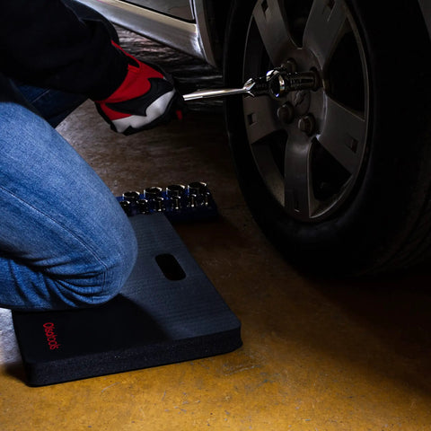 Mechanic Kneeling Pad With Thick High Density Foam near car tire, 18 x 11 x 1 inches, provides comfort for automotive repairs