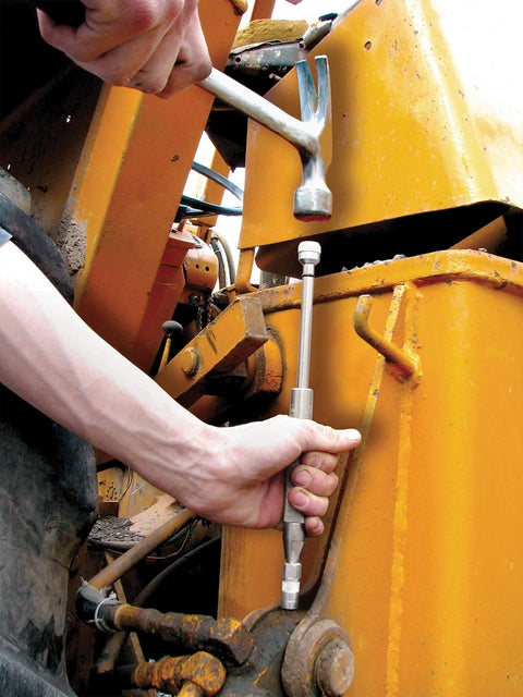 Grease joint rejuvenator kit used on yellow construction equipment; technician holds a long metal rod with a socket